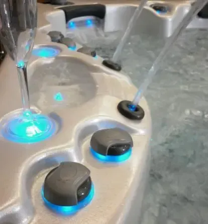 Close-up of a spa tub control panel with blue-lit buttons and water jets spraying into water