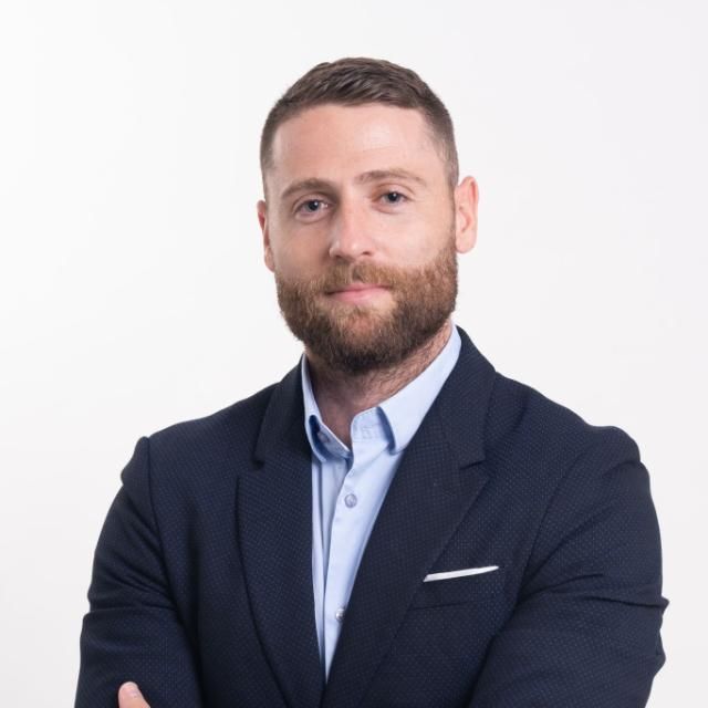 Portrait of a bearded man in a navy blazer and light blue shirt against a white background