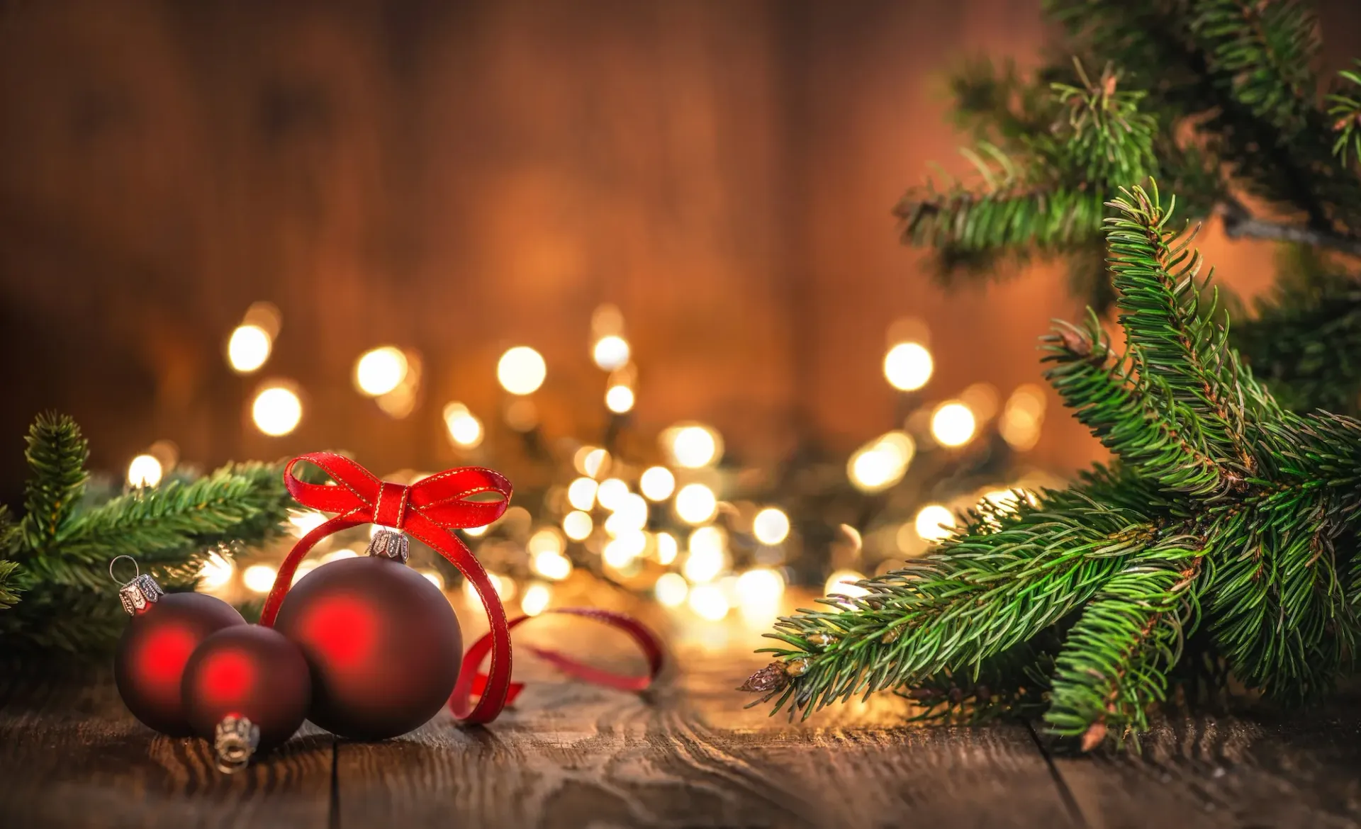 Red ball ornaments, strings lights and Christmas tree branch on a wood table
