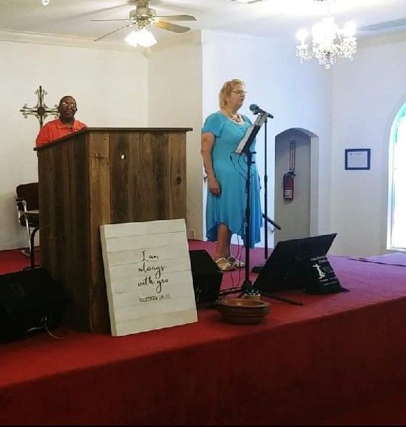 Woman in blue dress speaking at a microphone on a church stage beside a pulpit.