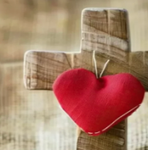 Red heart hanging on a wooden cross against a blurred beige background