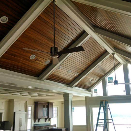 Interior with wood-paneled, vaulted ceiling, white trim, recessed lighting, ceiling fan, and view to a kitchen.