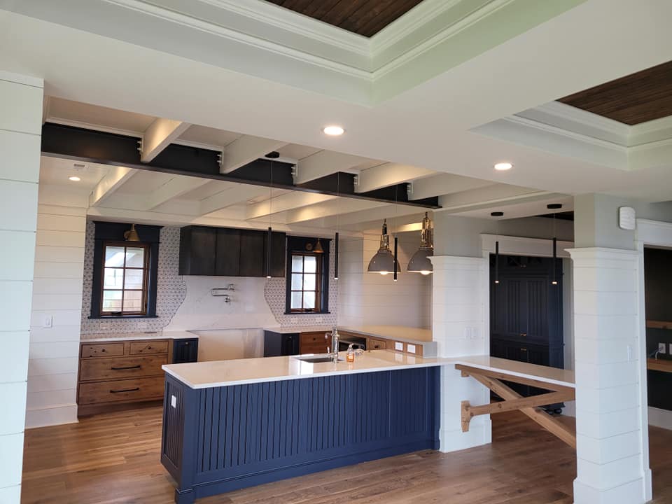 Spacious kitchen with blue island, dark cabinets, white countertops, wood beams, and pendant lights.