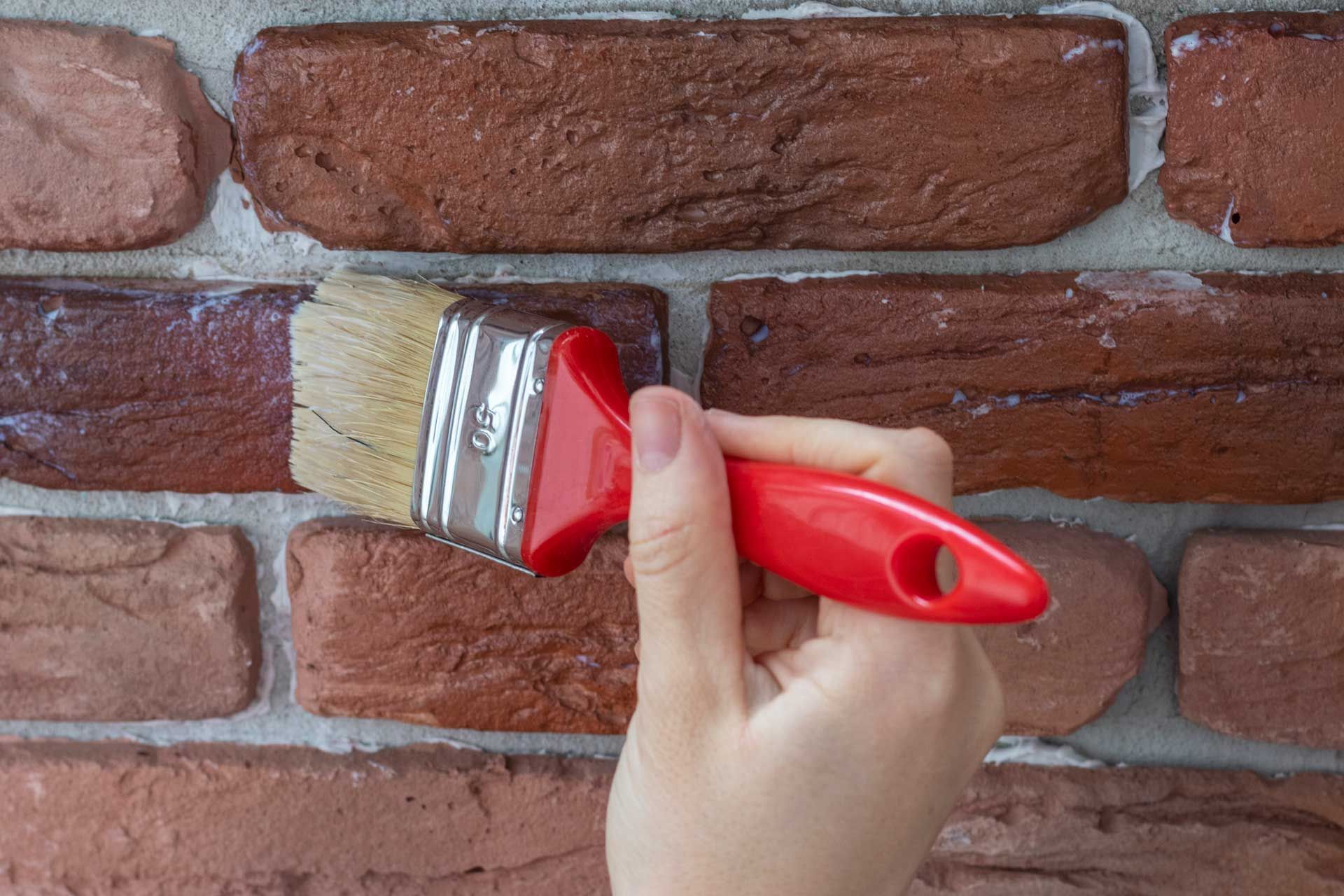 A person is holding a brush in front of a brick wall.