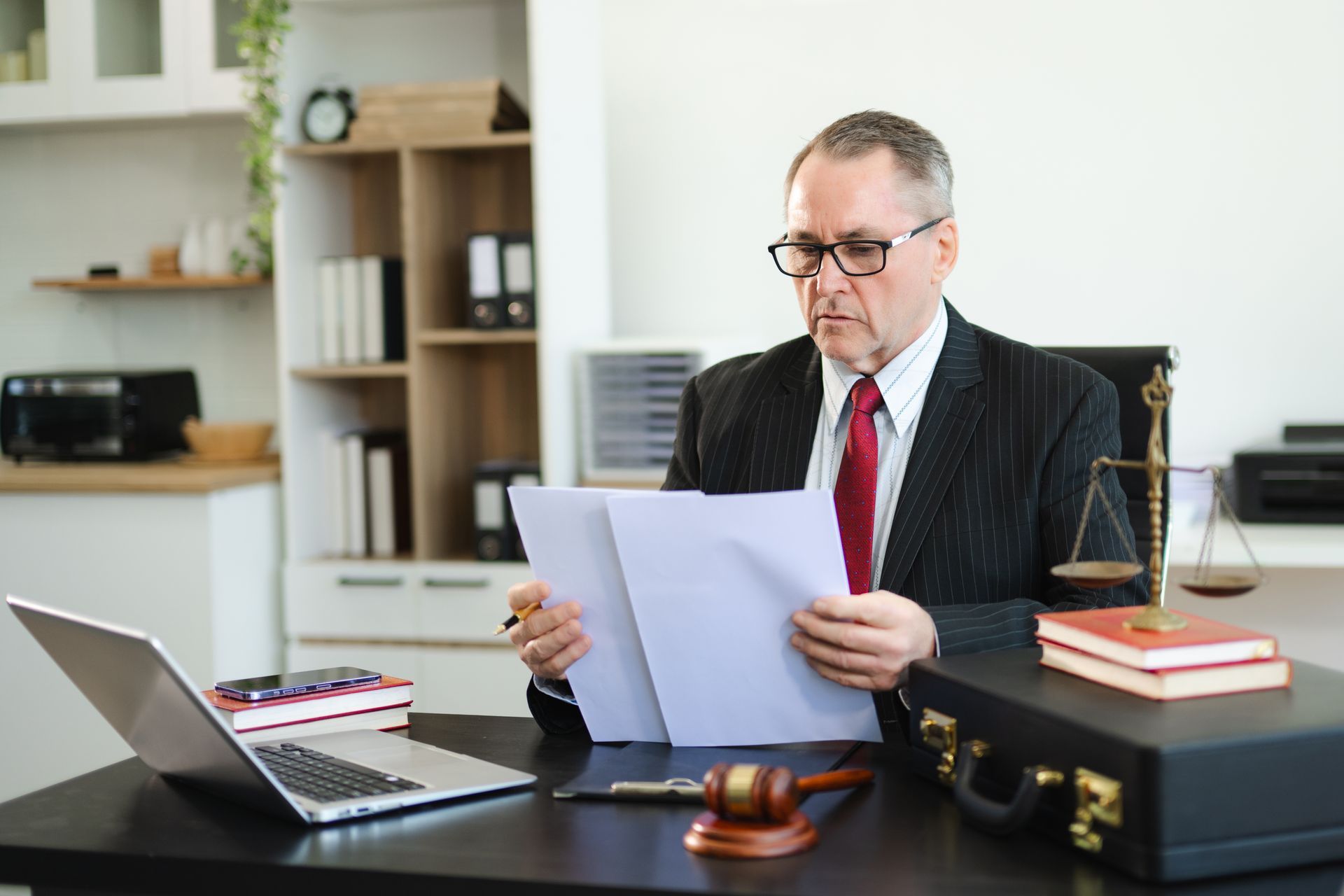 Man in suit reviewing documents at desk, gavel and scales visible.