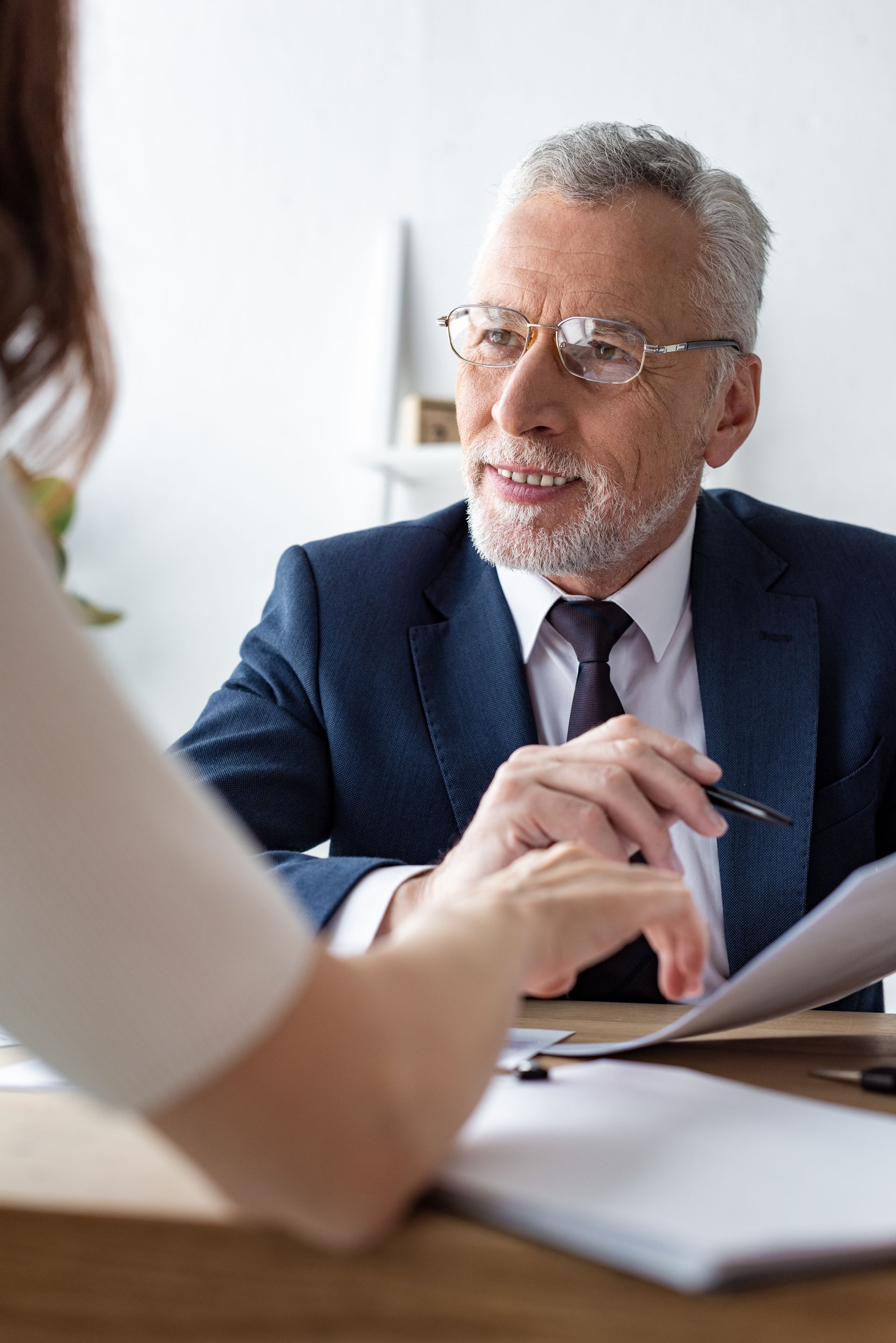 Man in suit reviews documents with person at a desk.