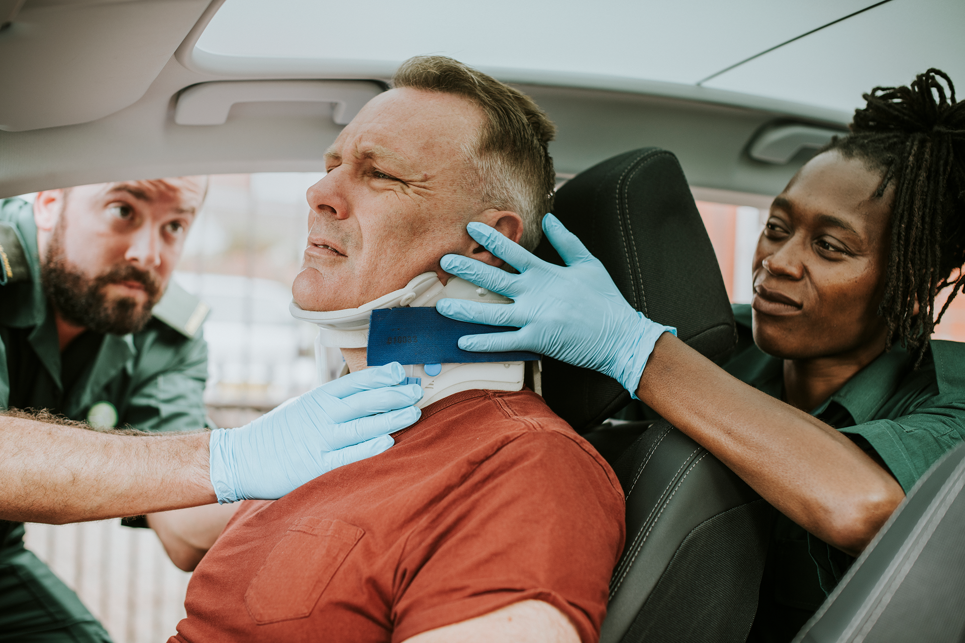 Paramedics stabilize patient's neck in car, applying a cervical collar.