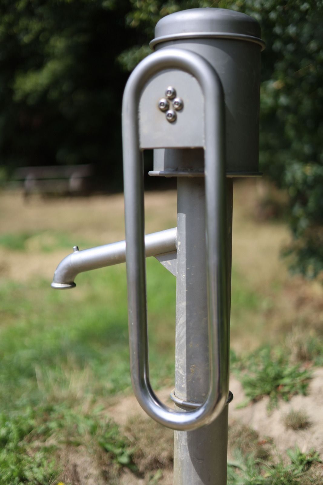 Close-up of a silver public water tap in a grassy park