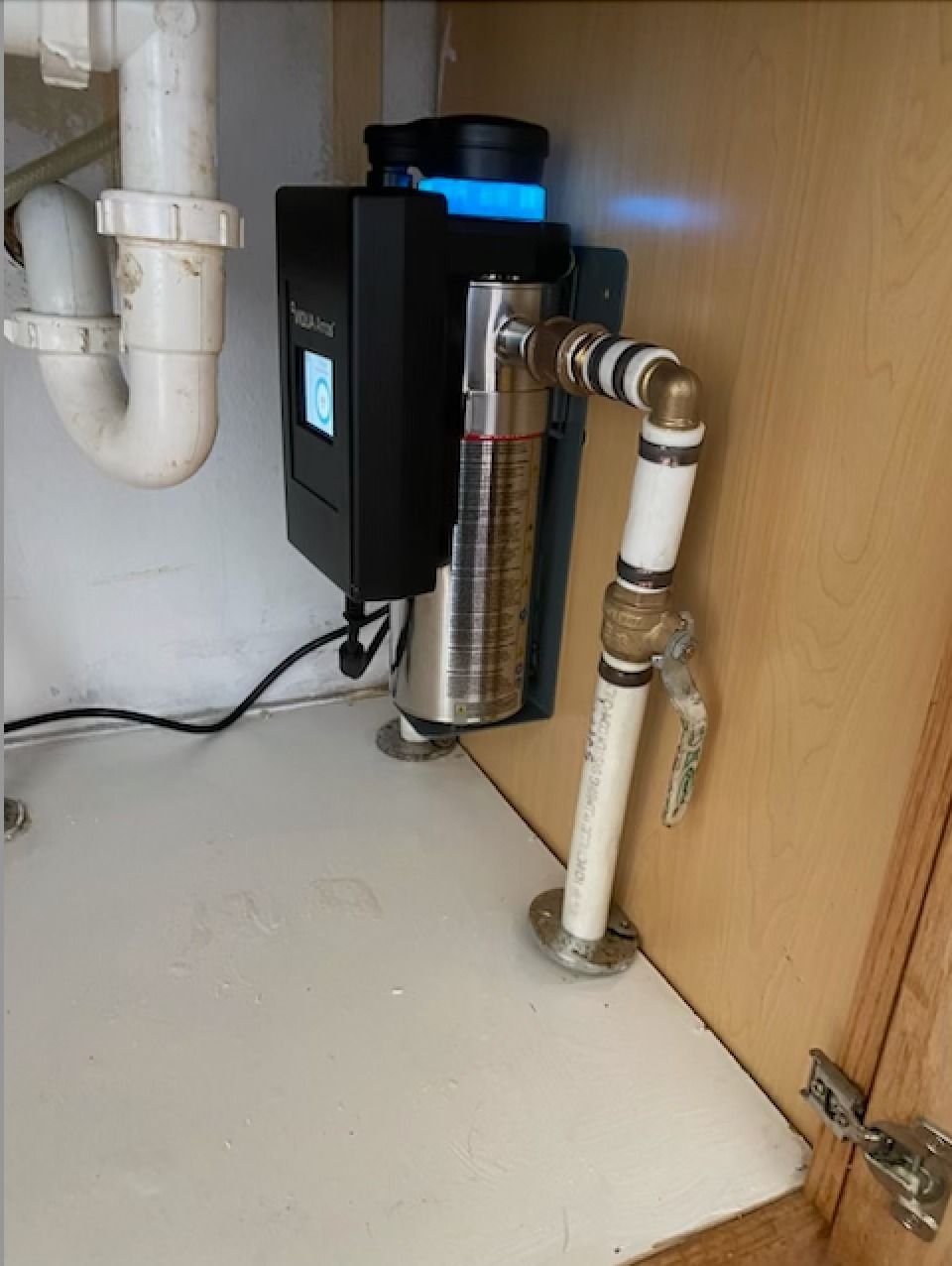 Under-sink water filtration system with black and stainless steel unit, pipes, and a blue indicator light