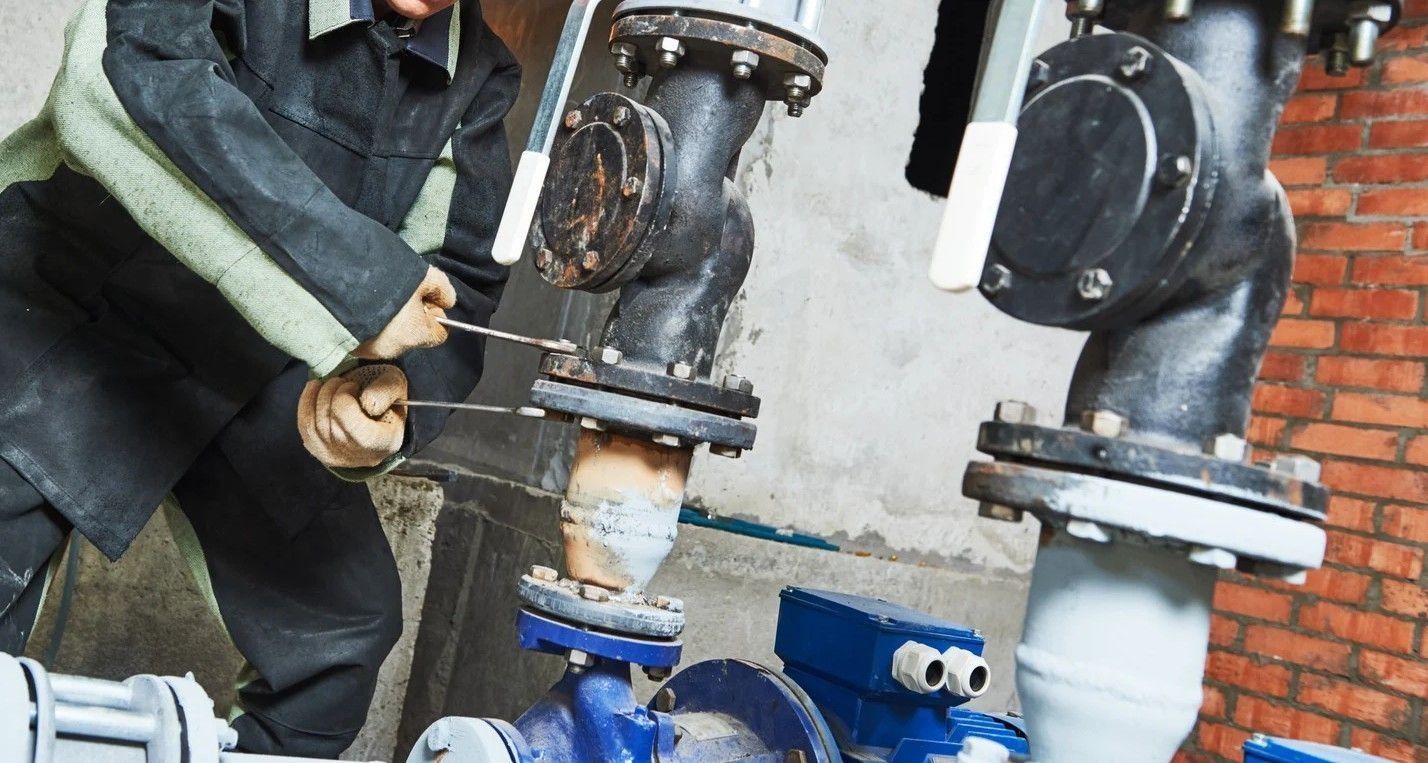 Worker repairing large industrial pipes with tools beside a brick wall