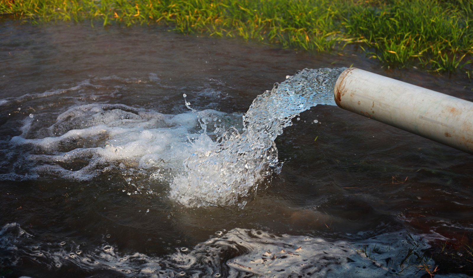 Water gushing from a white pipe into a dark stream with splashing ripples