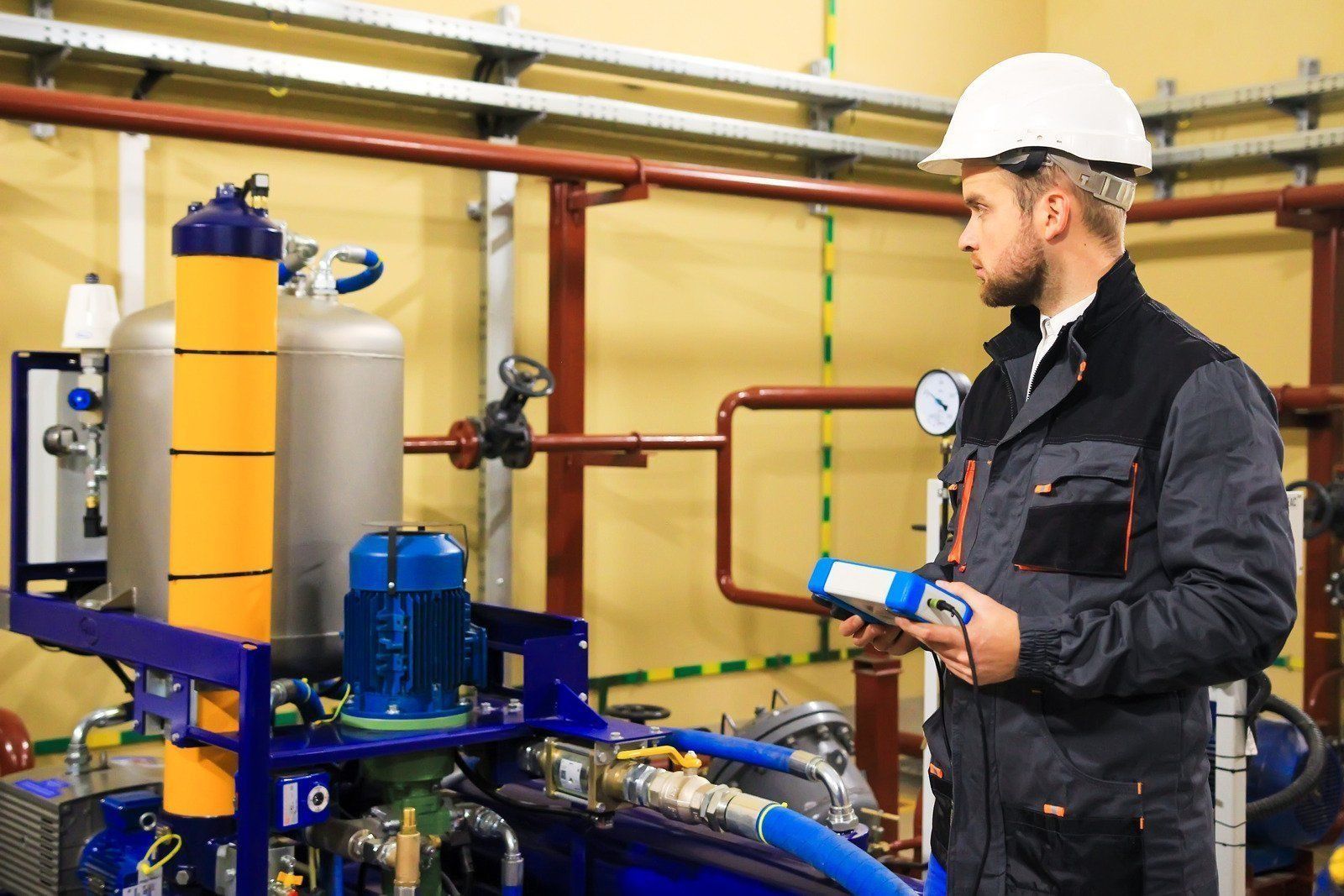 Under-sink water filtration unit with black housing, blue light, and connected pipes in a cabinet