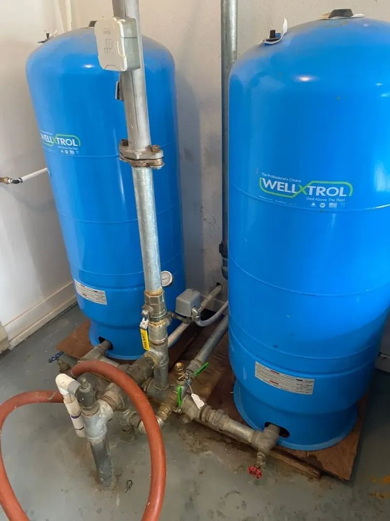Two blue industrial water tanks with pipes and valves in a utility room