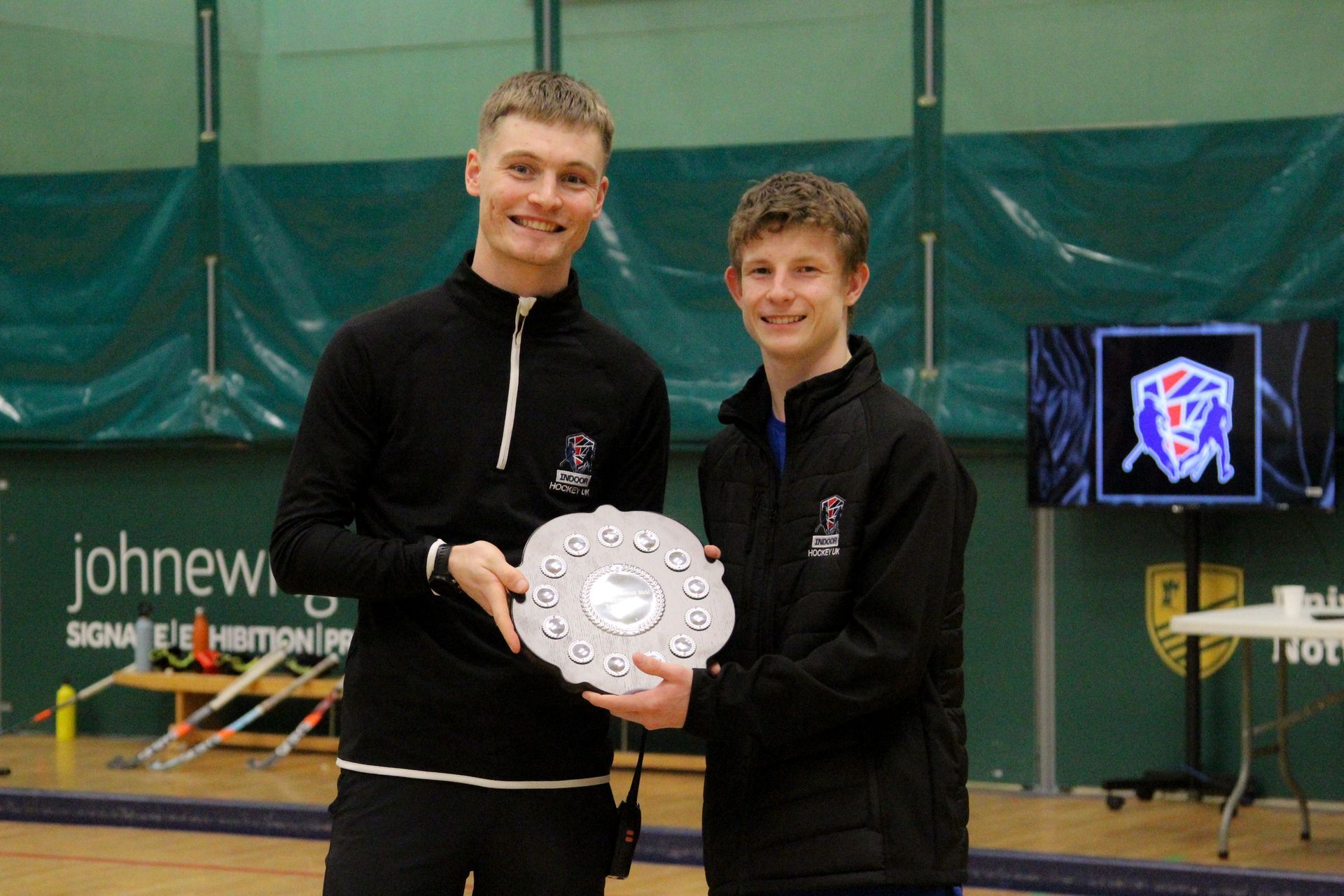 Two people holding Derrick Hall Memorial Sheild in an indoor sports hall