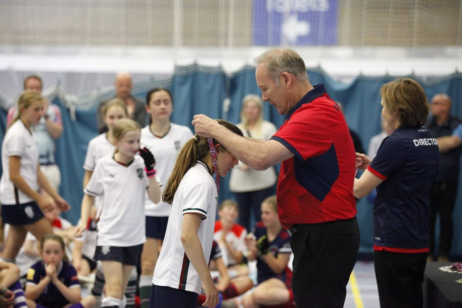 Presenter placing a medal around a child’s neck at an indoor sports event