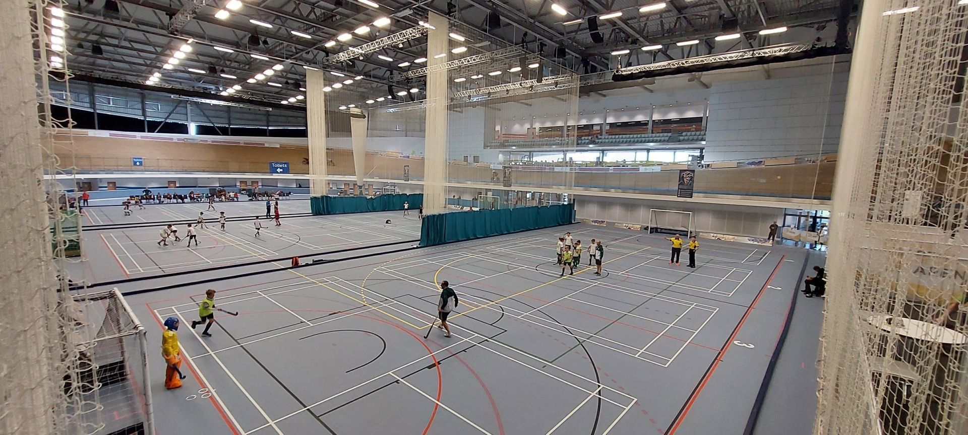 Indoor sports hall with several people practicing on marked court lanes under bright ceiling lights