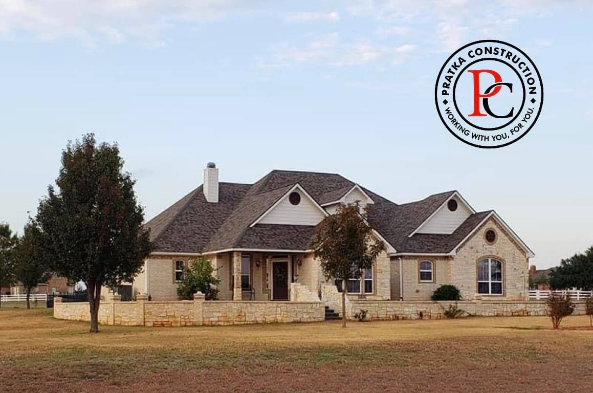 Large, light-colored stone house with brown roof, in a grassy field. 