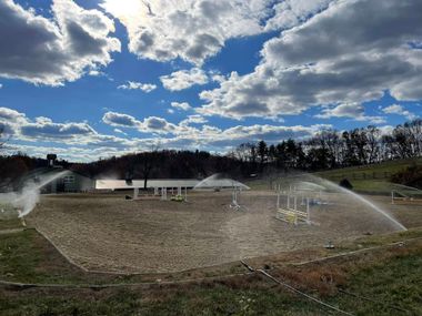 Sprinklers watering a barren field under a partly cloudy blue sky