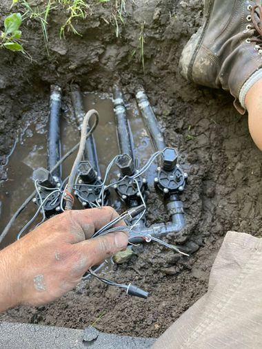 Utility worker exposing underground cable connections in a dirt trench, with gloved hand and pipes visible.