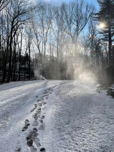 Snow-covered road with footprints and drifting snow in a wooded area at sunrise