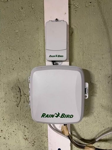 Rain Bird irrigation controller mounted on a textured wall, with wiring visible below.