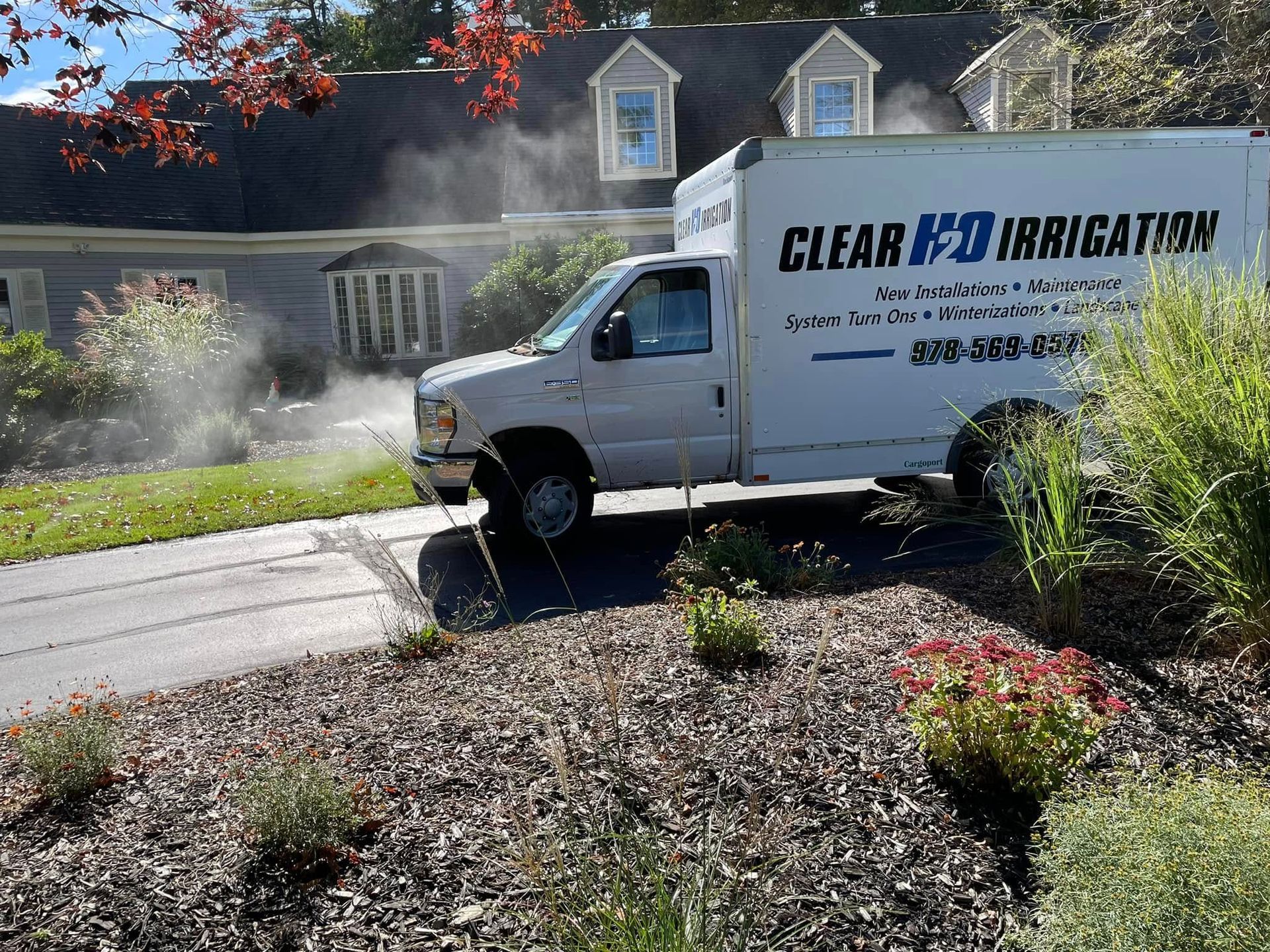 Irrigation service truck spraying water in a suburban yard beside a house