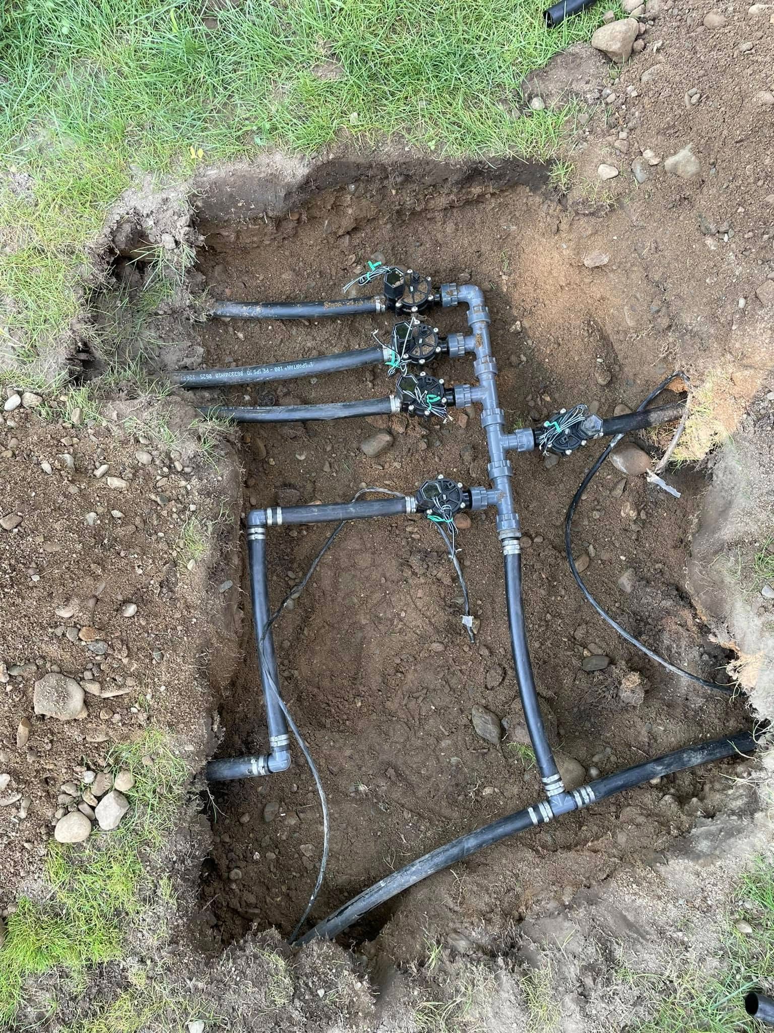 Trench with blue irrigation pipes and fittings laid in exposed soil outdoors
