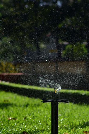 Sprinkler spraying water across a green lawn in front of a tan building at sunset