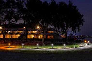 Nighttime view of a lit building with trees and path lights along a grassy lawn
