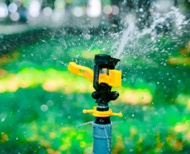 Yellow sprinkler spraying water in a green garden against a blurred background