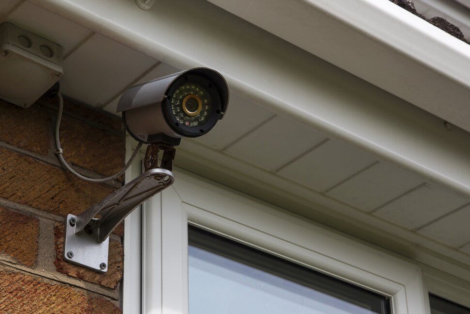 A security camera is sitting on top of a pole in front of a building.