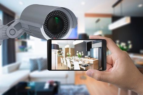 A person is holding a cell phone in front of a security camera in a living room.