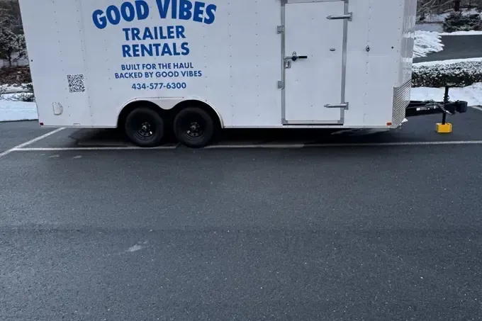 White Good Vibes trailer parked on a wet road in snowy weather, with black lettering and yellow hitch.