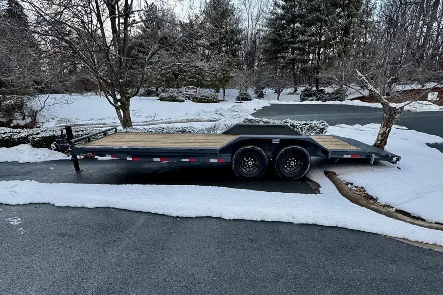 Snow-covered flatbed trailer parked beside a driveway in a winter yard.