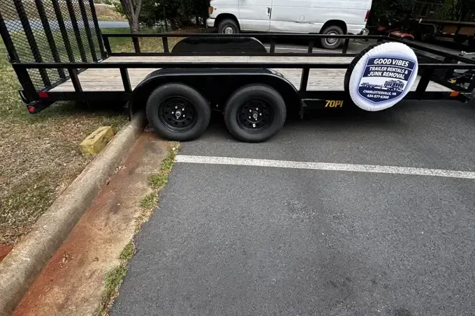 Black utility trailer parked by a curb, with two wheels and a white circular sign on the side.