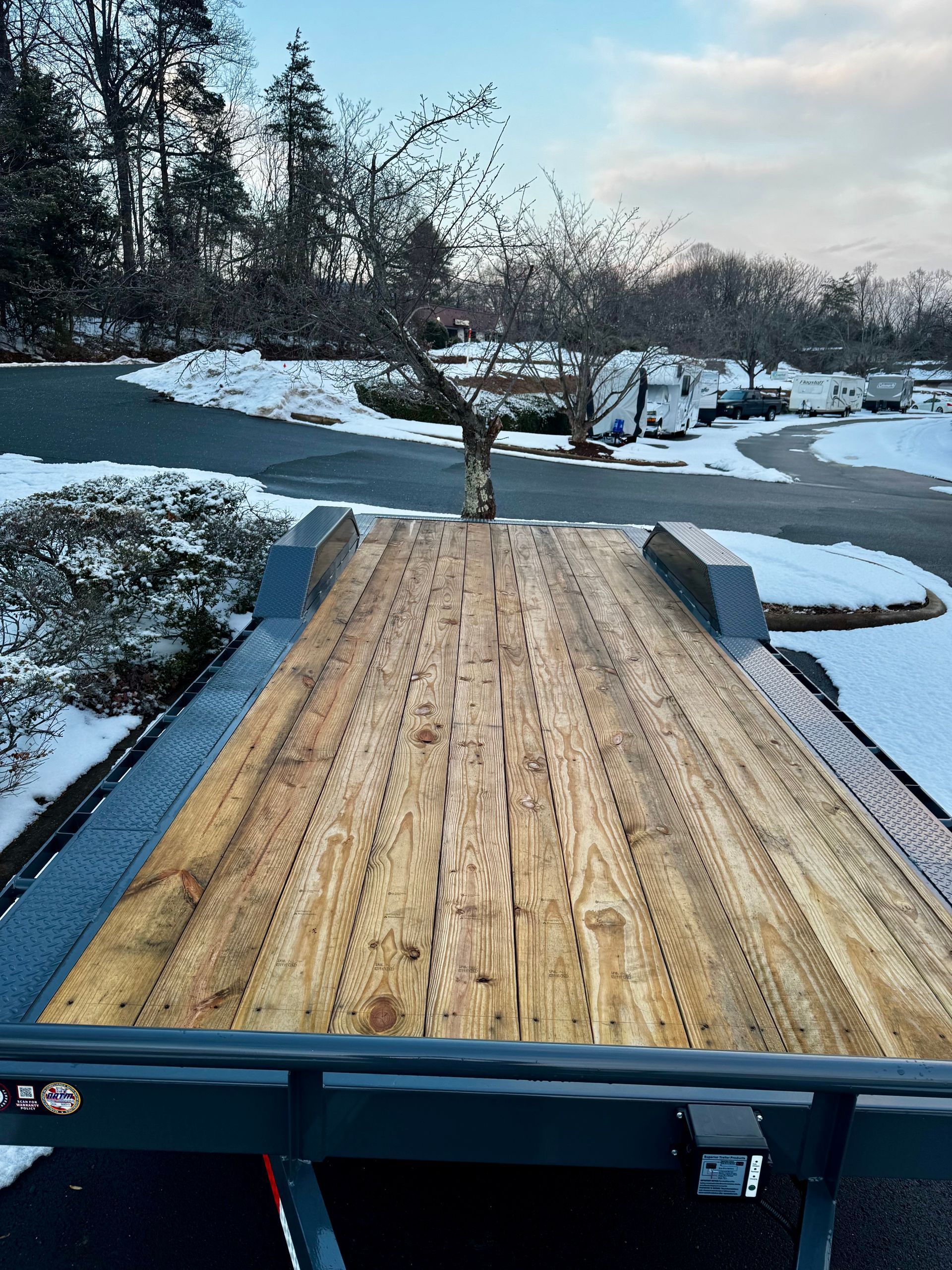 Wooden trailer bed overlooking a snowy driveway and leafless trees in winter