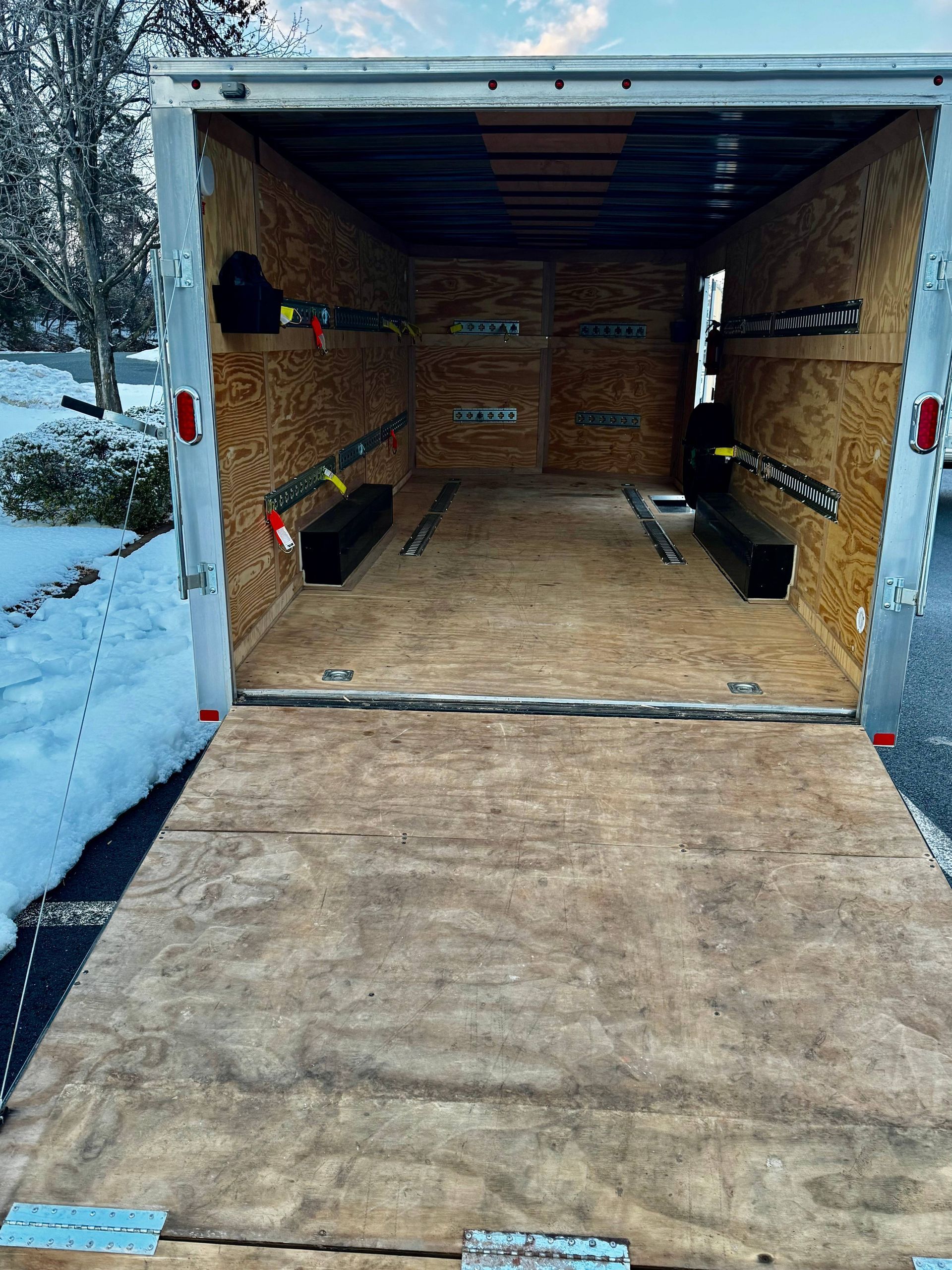 Snow-covered enclosed trailer with wooden interior and loading ramp open outside