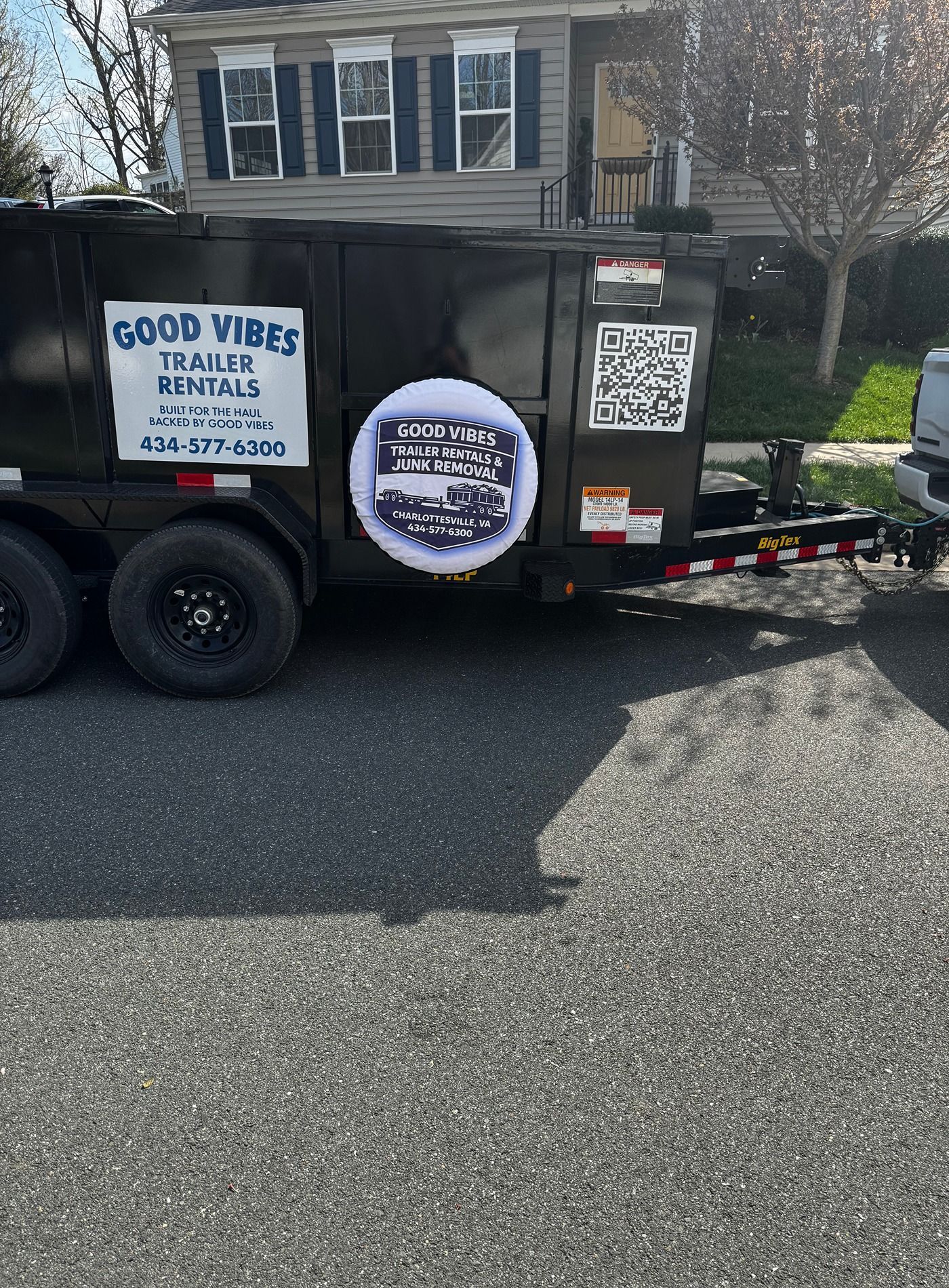 Black dump trailer with “Good Vibes” signs parked in a residential driveway.