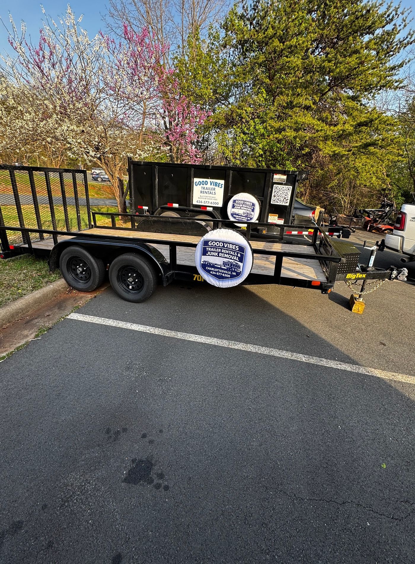Black utility trailer with large round sign parked beside a road and trees in daylight