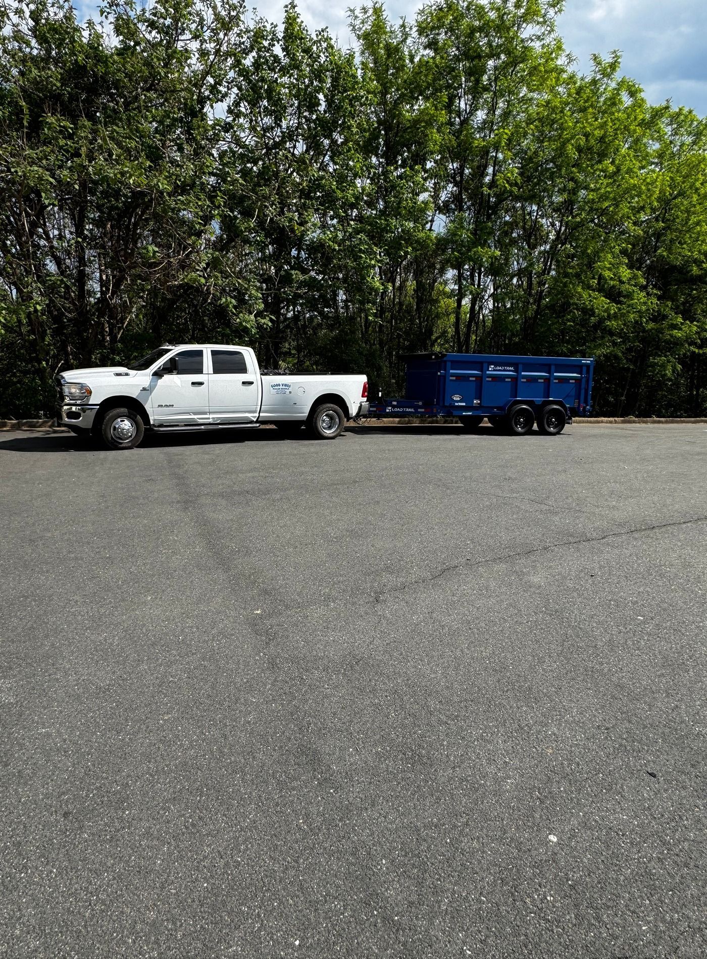 White pickup truck towing a blue trailer on a gravel lot with trees in the background