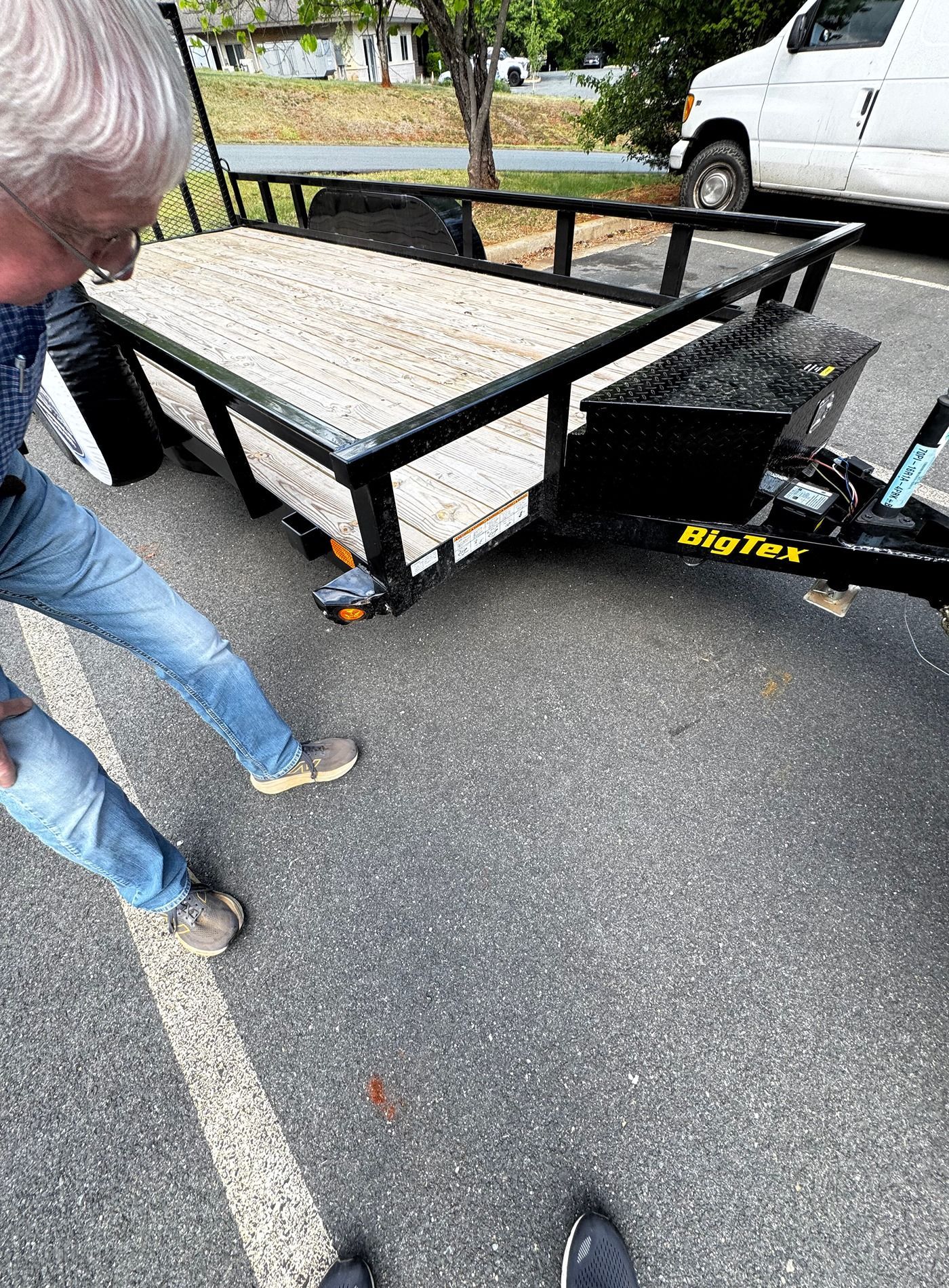 Metal utility trailer with a ramp parked on pavement, with a person standing beside it