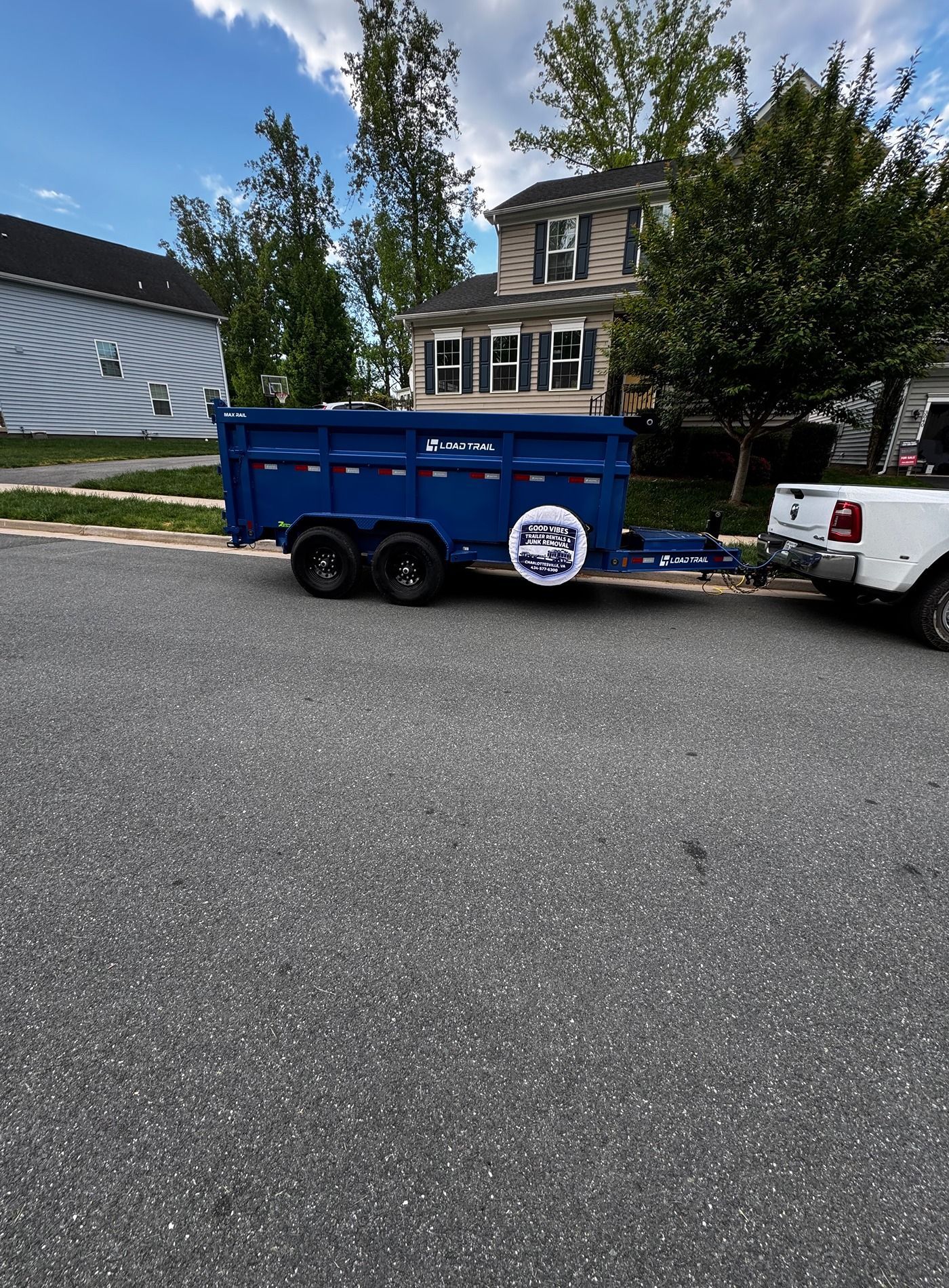Blue utility trailer parked on a street in front of a house, hitched to a white pickup truck.
