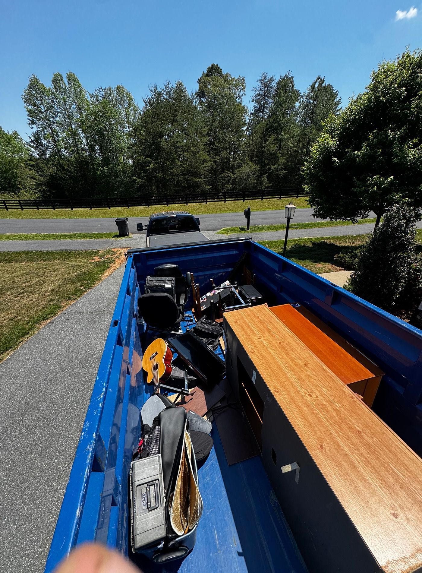 Blue truck bed loaded with tools and lumber, parked by a roadside under a sunny sky