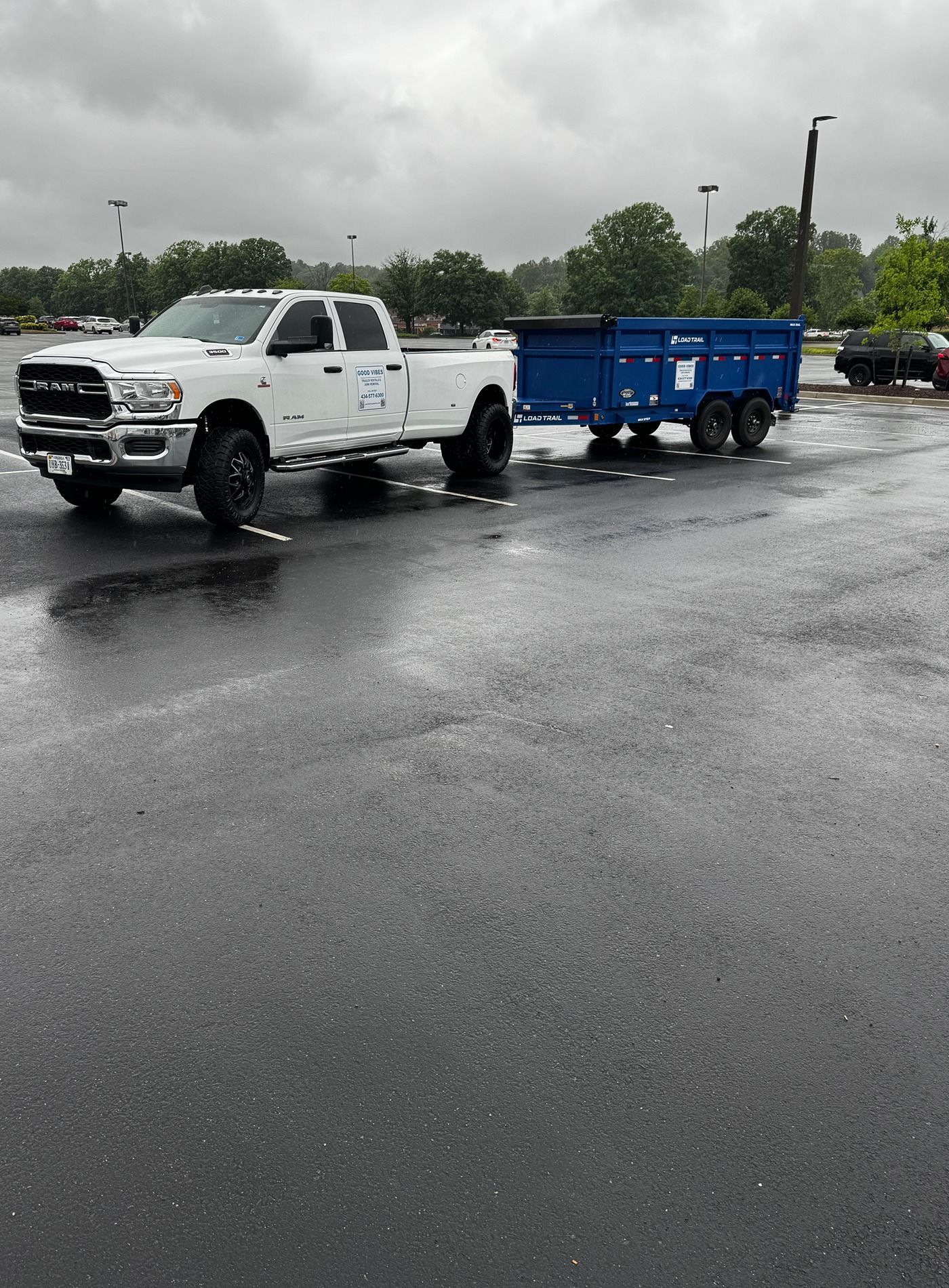 White pickup truck towing a blue trailer in a wet parking lot