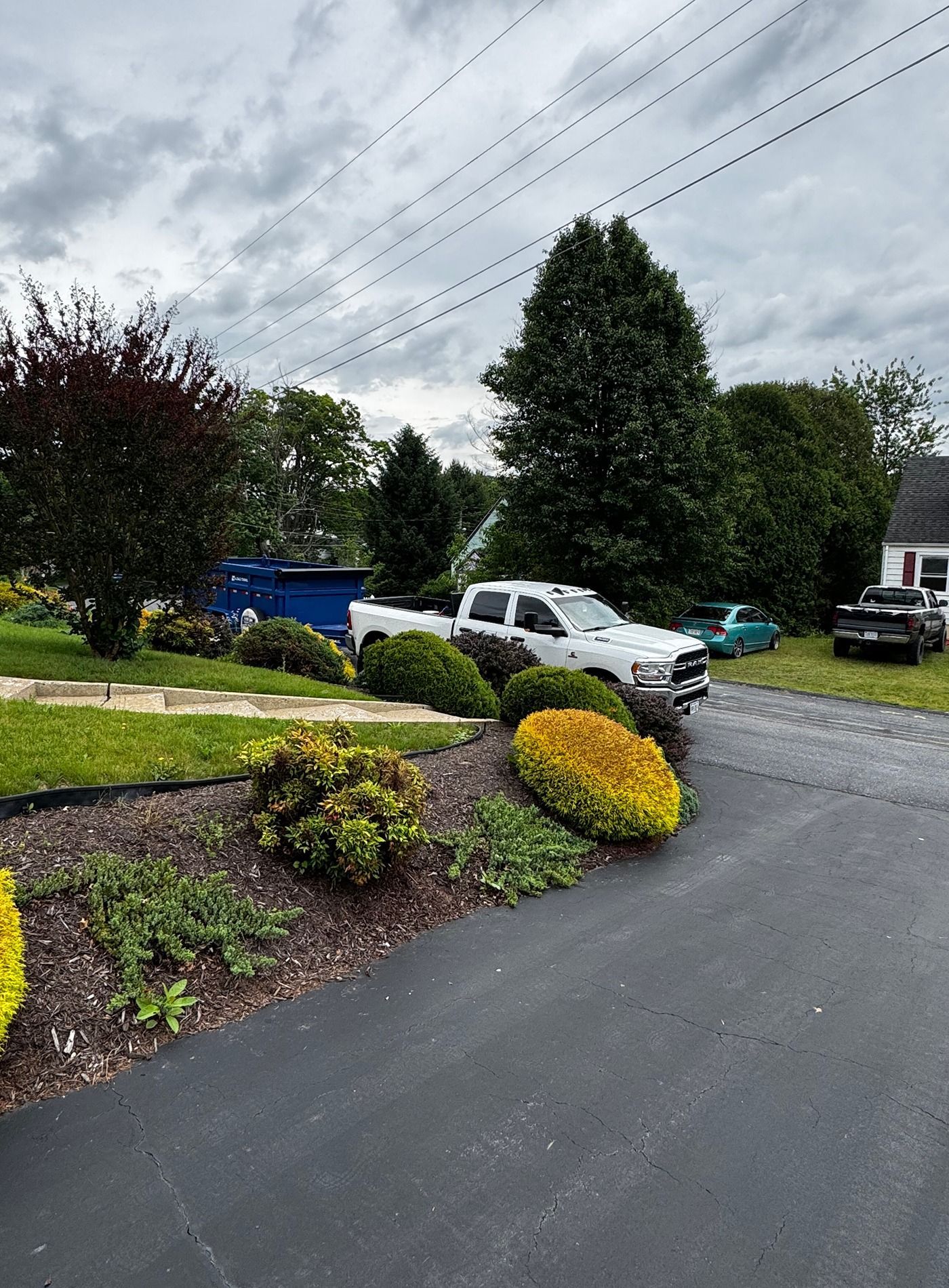 White SUV parked on a driveway beside landscaped shrubs under a cloudy sky