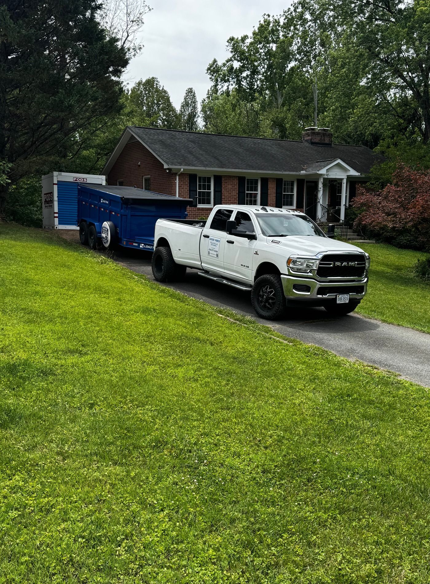 White pickup truck and blue trailer parked in a driveway in front of a brick house.