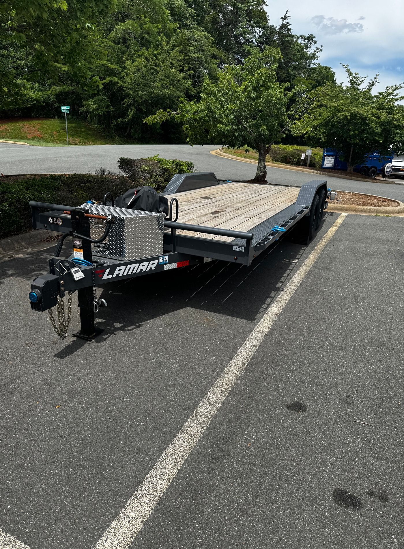 Flatbed trailer parked in a lot, with a metal toolbox and ramps on the front.