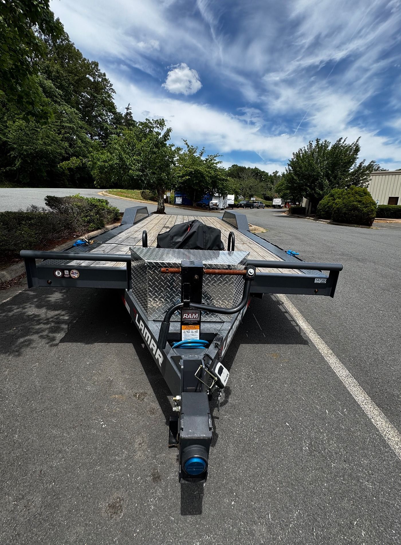Empty flatbed trailer parked on a road under a cloudy blue sky