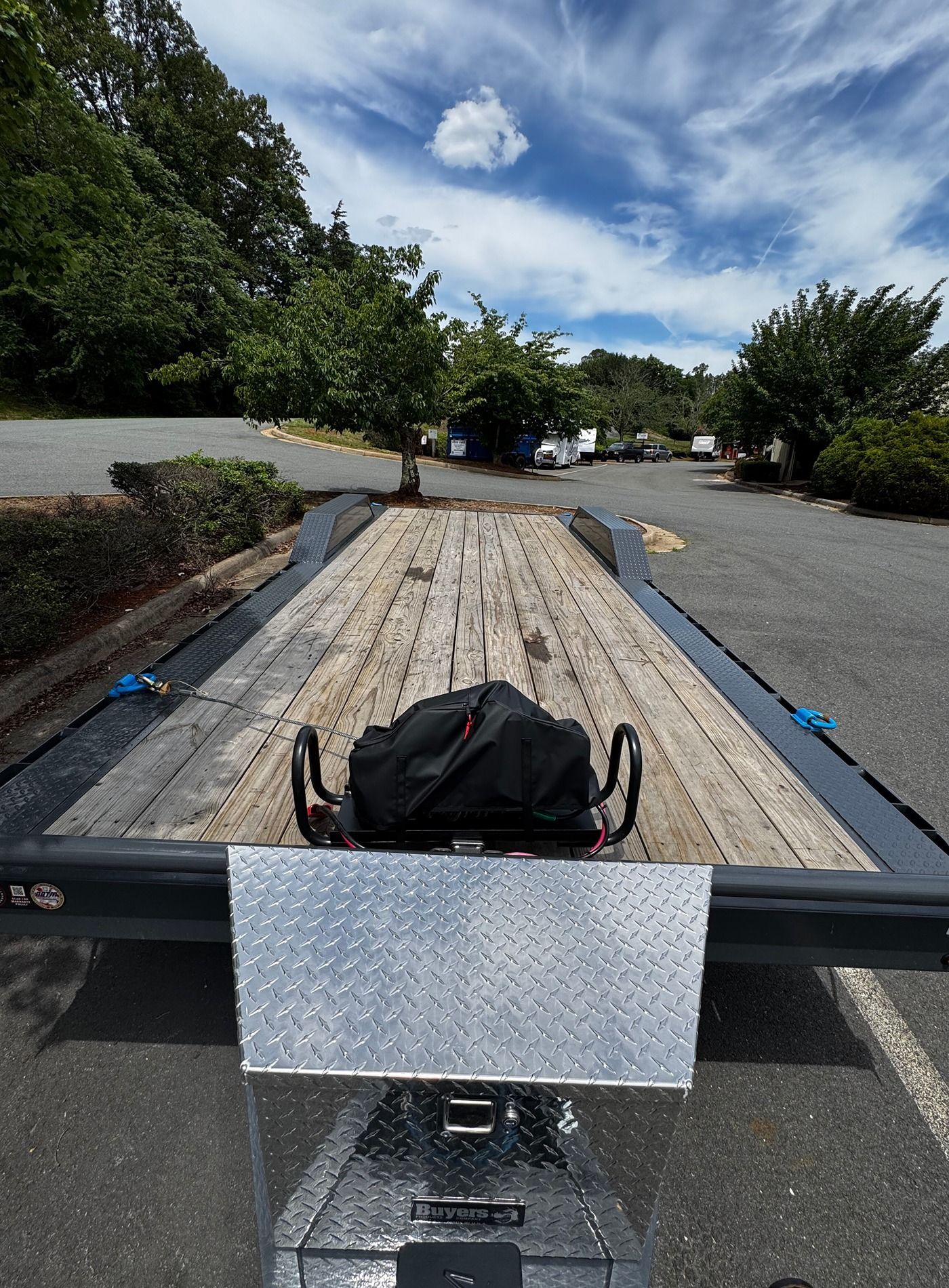 Rugged utility trailer loaded with a wooden plank, parked on a paved road under a blue sky