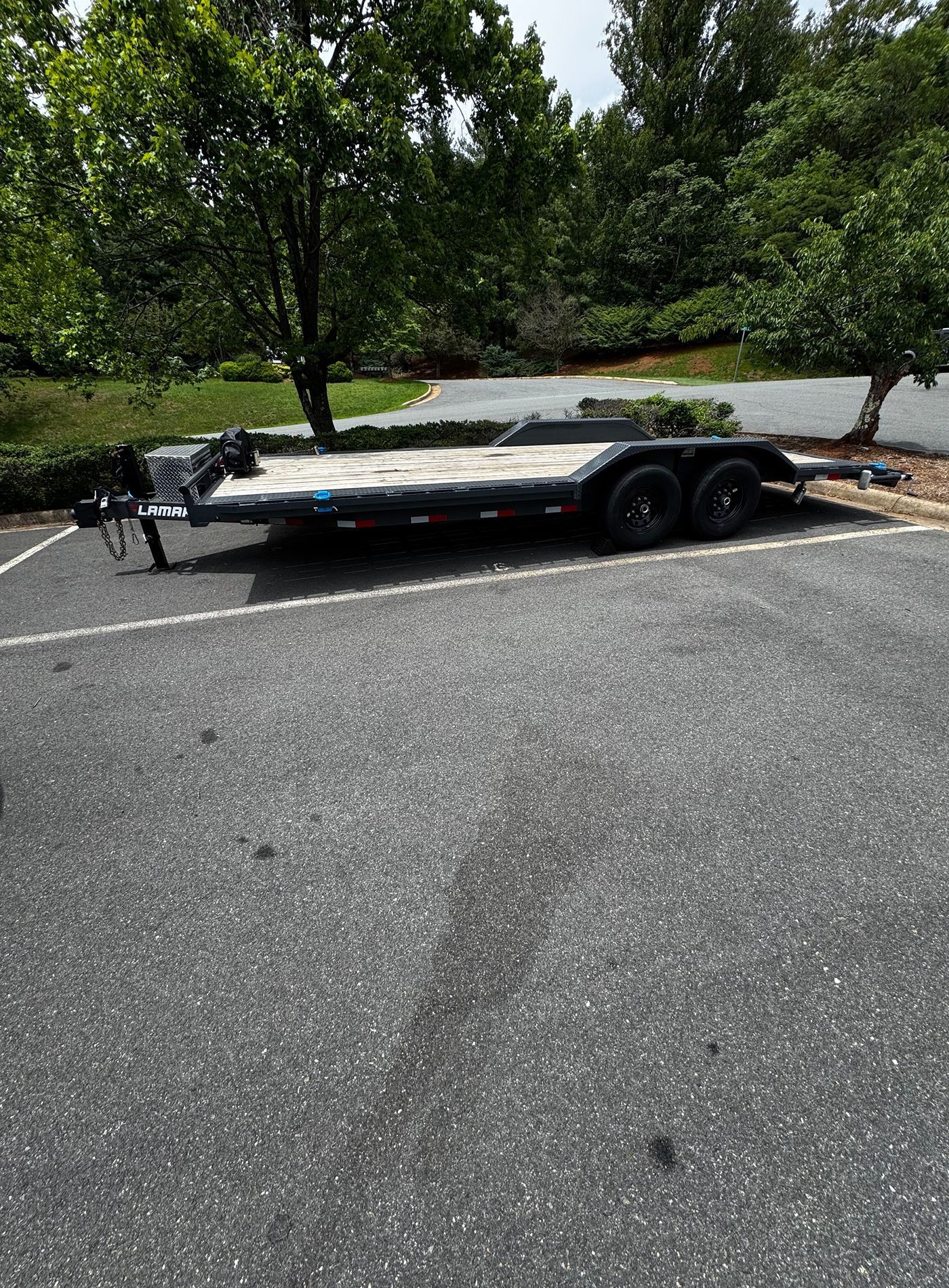 Flatbed trailer parked on a paved roadside near trees and a curb stop.